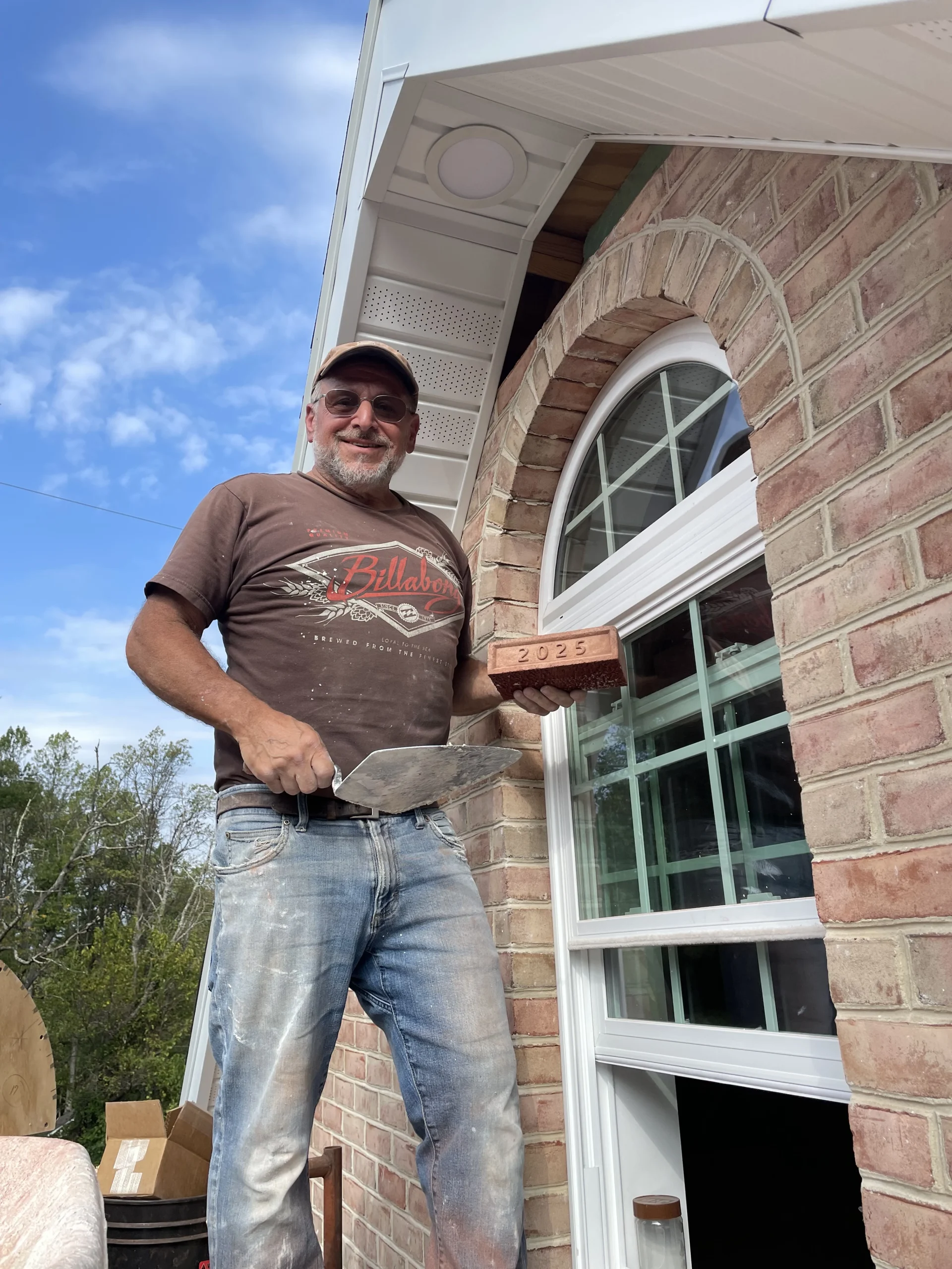 Dave standing outside with masonry tools and a 2025 commemorative brick